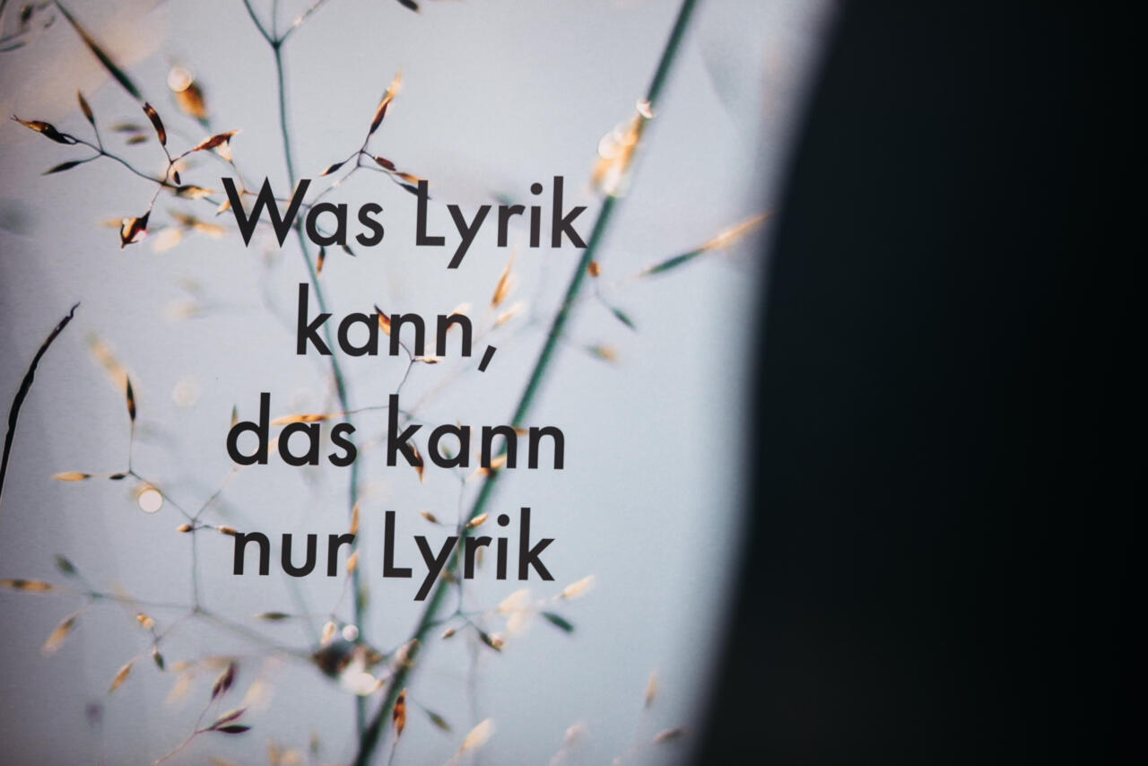 Ausschnitt eines Tisches mit Krokodilklemmenkabeln, einer LED und verschiedenen Materialien, Strohhalm, Stein, Holzstab. Zwei Kinder sitzen am Tisch. Eines schließt die Krokodilklemme an den Strohhalm an.