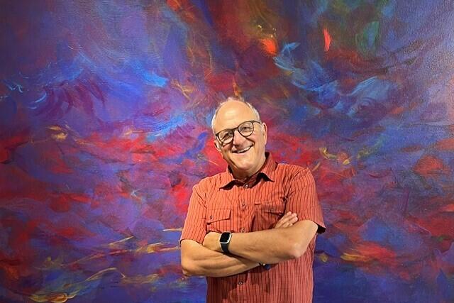 Halbkörperportrait von Stefan Ruppaner, der mit freundlichem Lächeln und verschränkten Armen vor einer abstrakt bunt bemalten Wand steht.