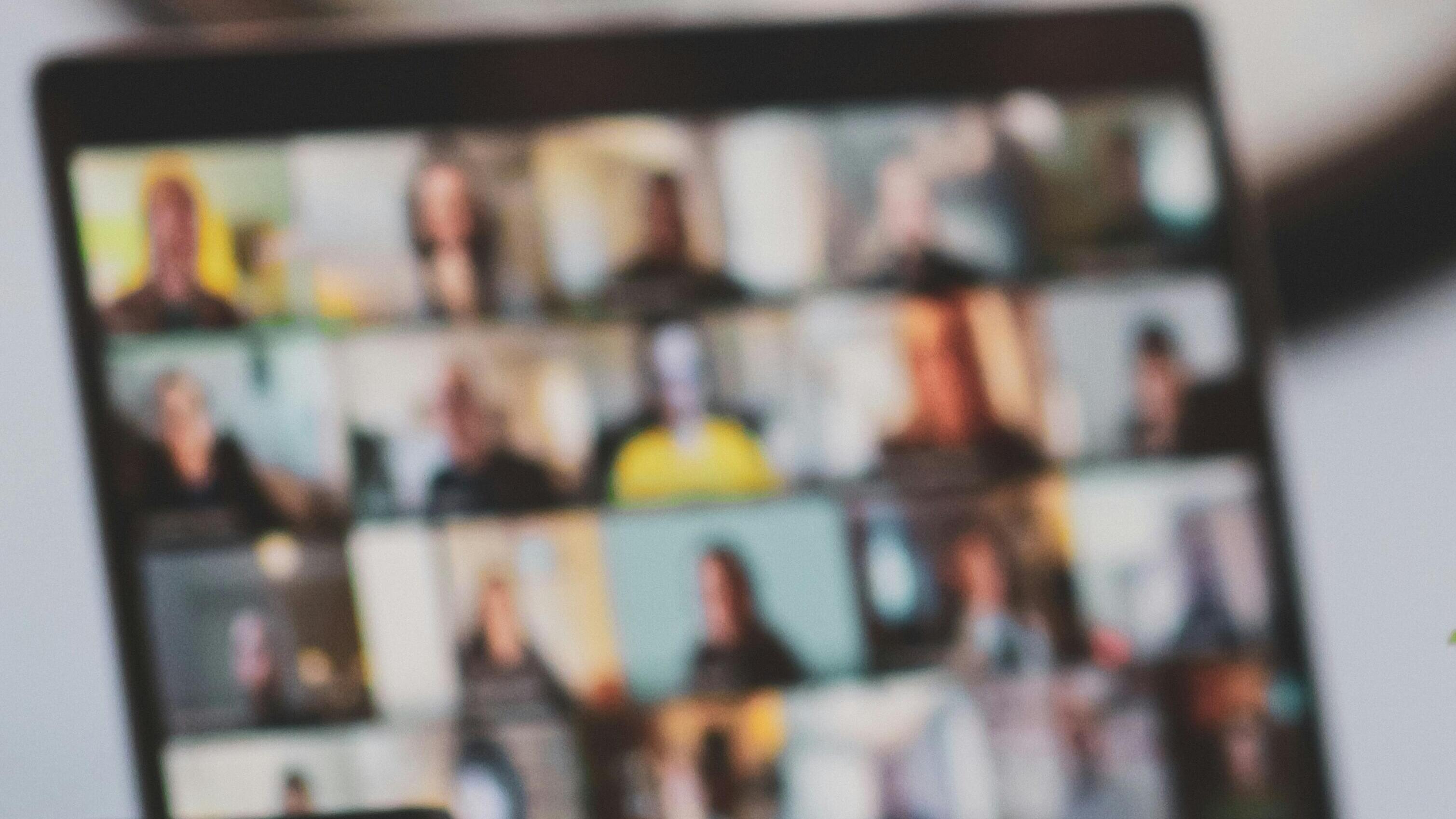 Unscharfe Aufnahme eines Notebooks, auf dessen Bildschirm eine Onlineveranstaltung mit mehreren Teilnehmenden in einer Videokonferenz zu sehen ist.
