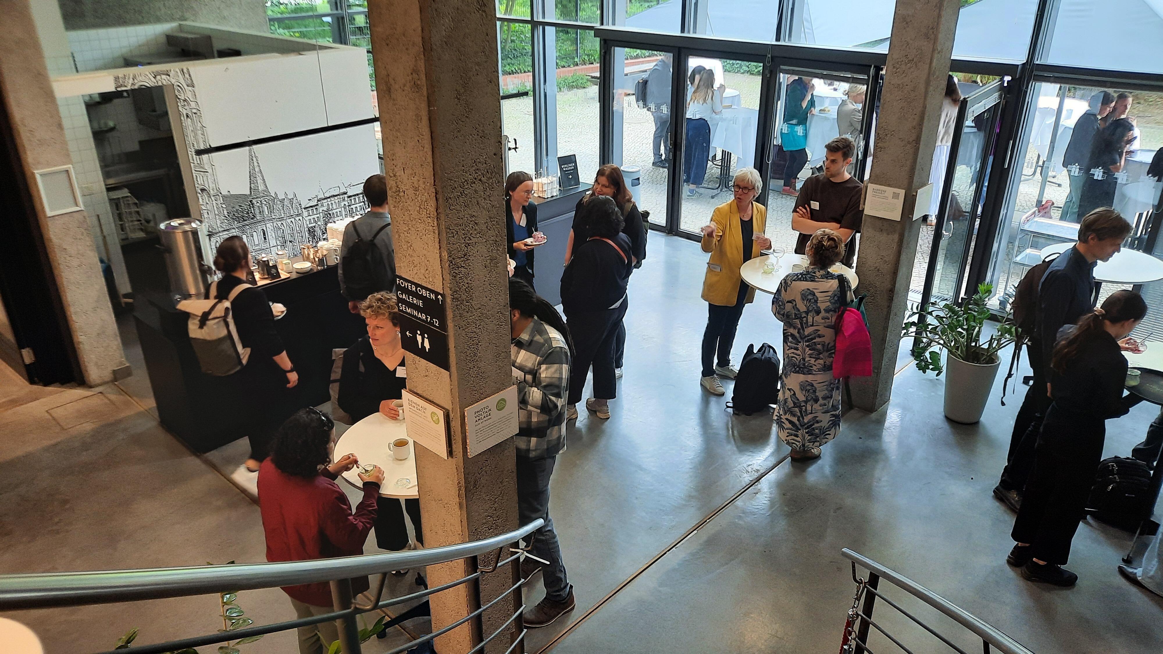 Teilnehmende tauschen sich vor Beginn der Vernetzungstagung im Empfangsbereich des Umweltforums Berlin aus.