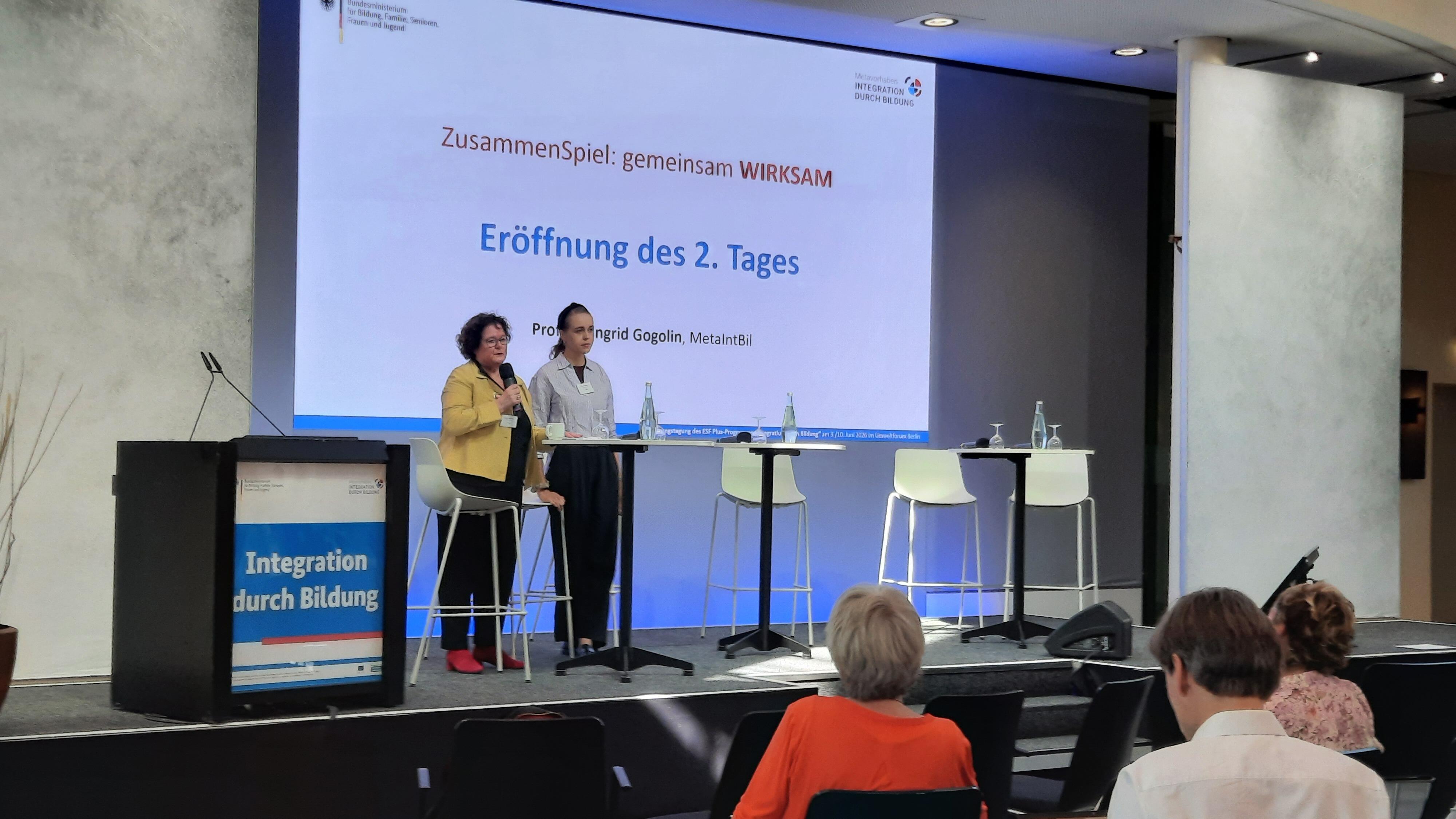 Prof. Dr. Dr. h.c. Ingrid Gogolin und Anouk Ticheloven auf einer Bühne vor einem Stehtisch.