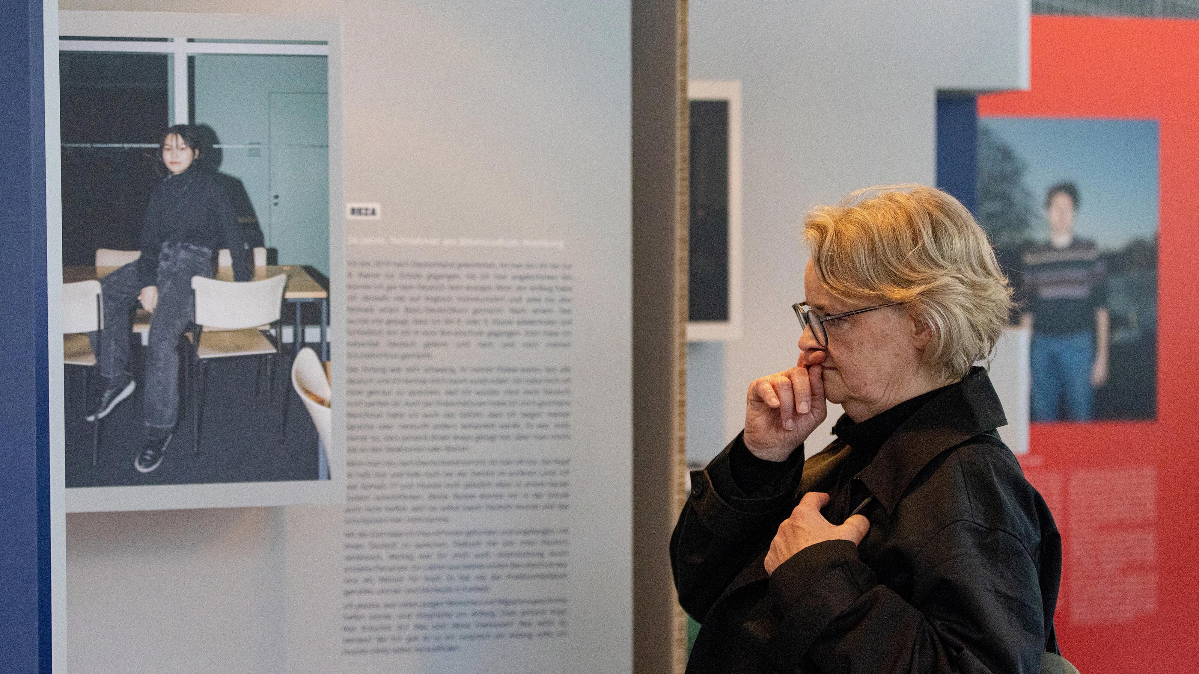 Eine Dame steht vor einer Ausstellungstafel der Wanderausstellung "Bildungswege in der Migrationsgesellschaft".