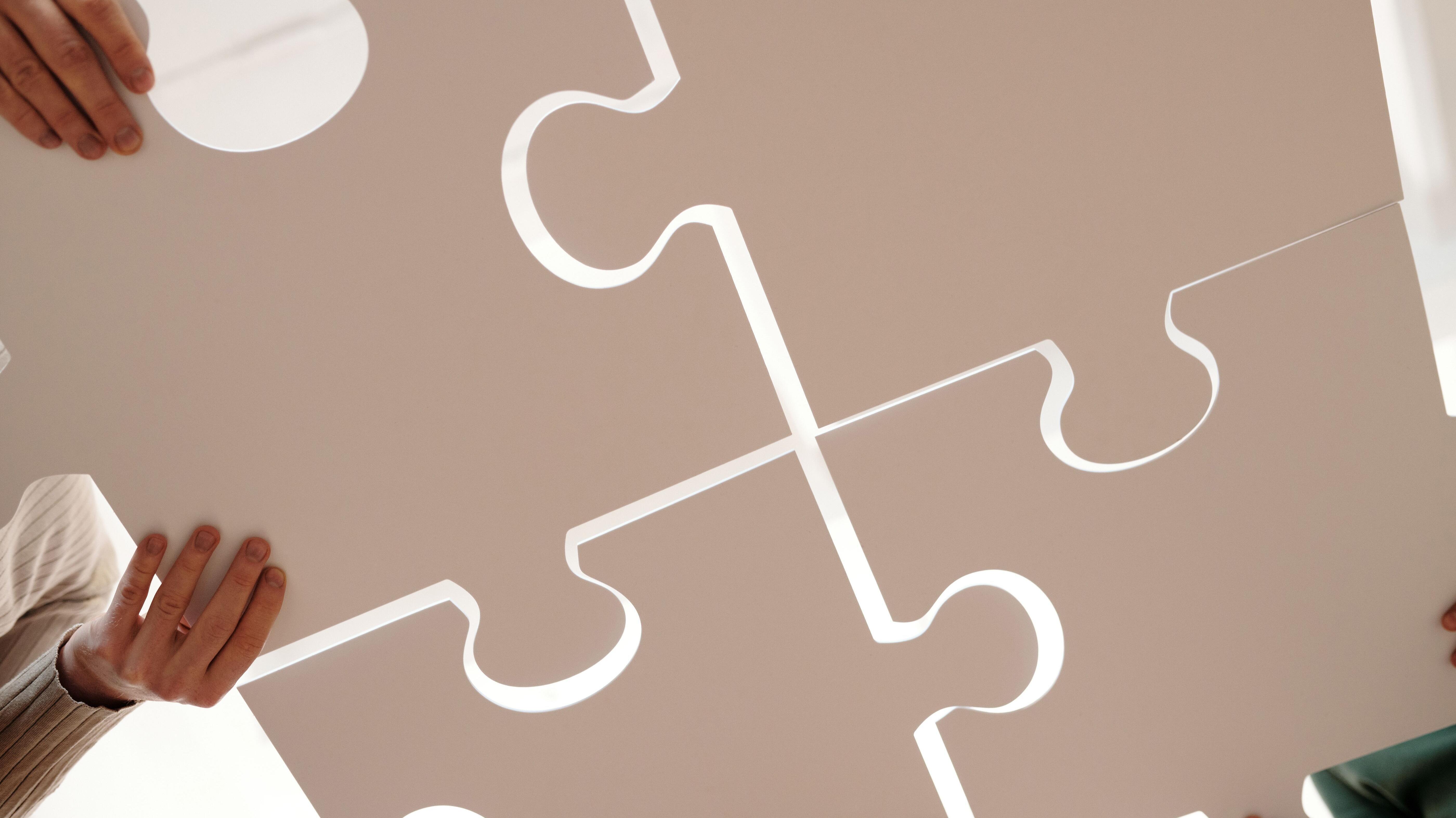 Vier große Puzzleteile werden von mehreren Händen zusammengefügt.