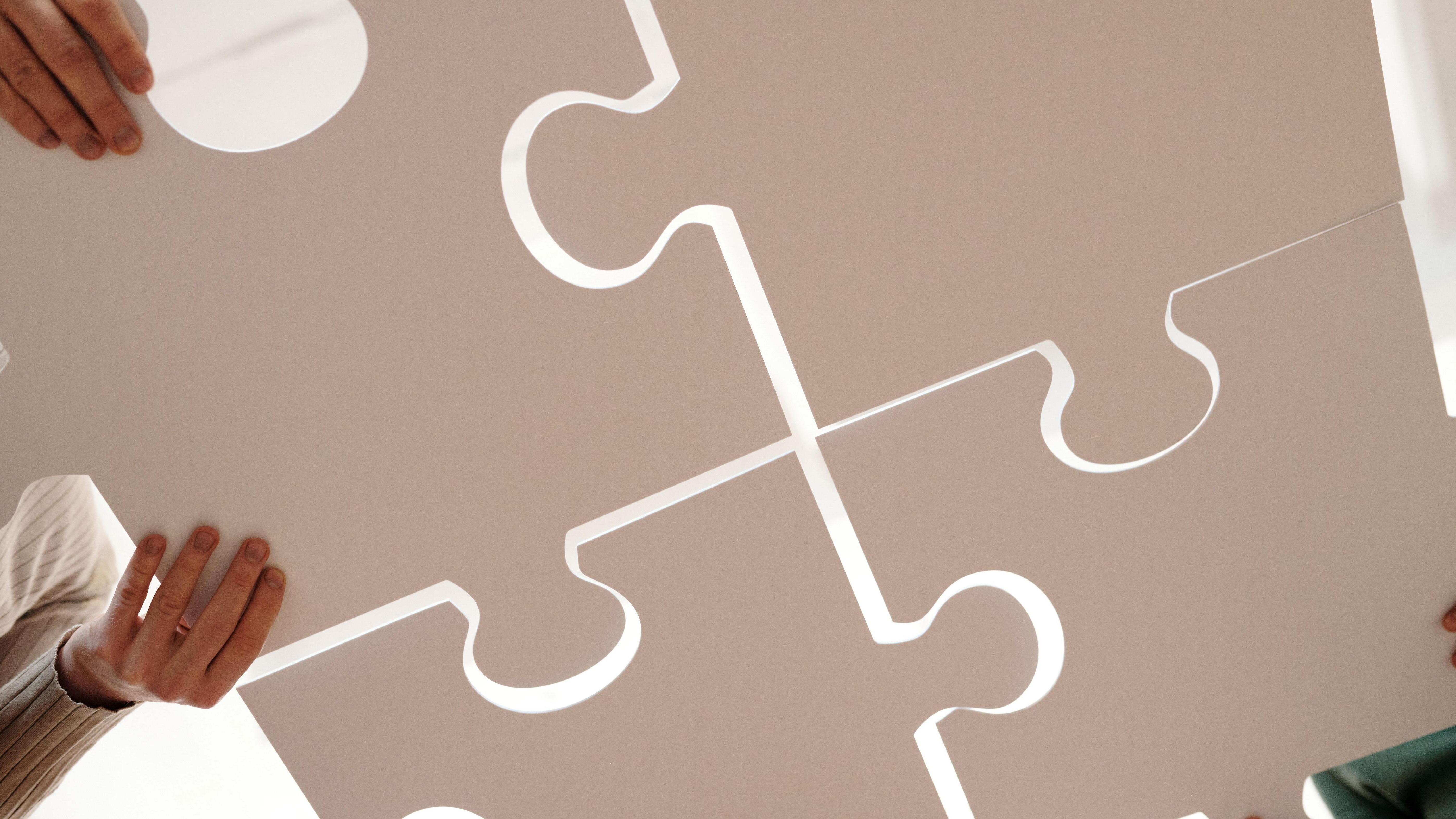 Vier große Puzzleteile werden von mehreren Händen zusammengefügt.