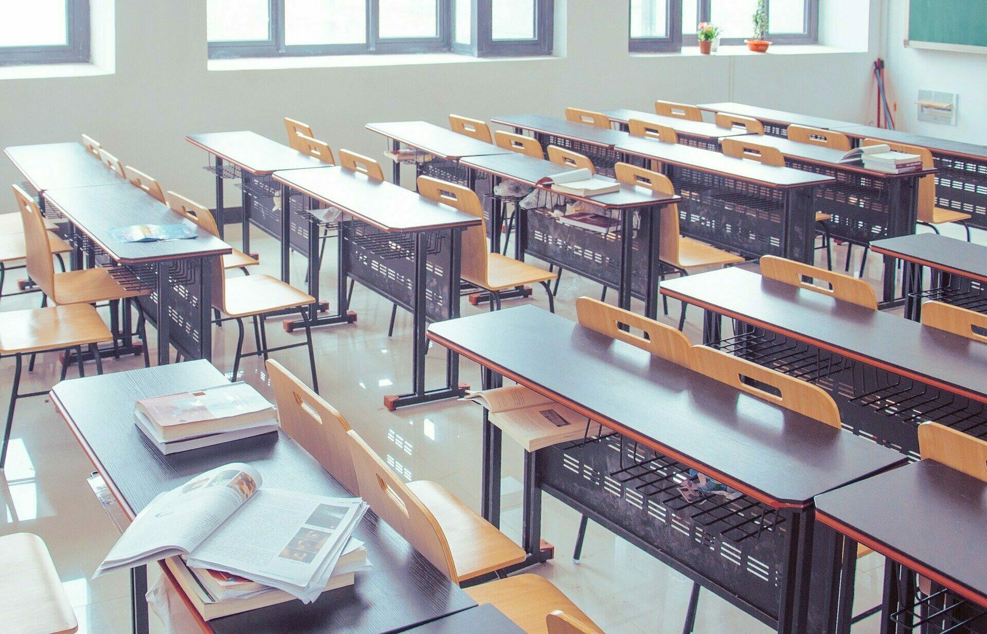 Klassenzimmer mit Tischen, Stühlen und Tafel.