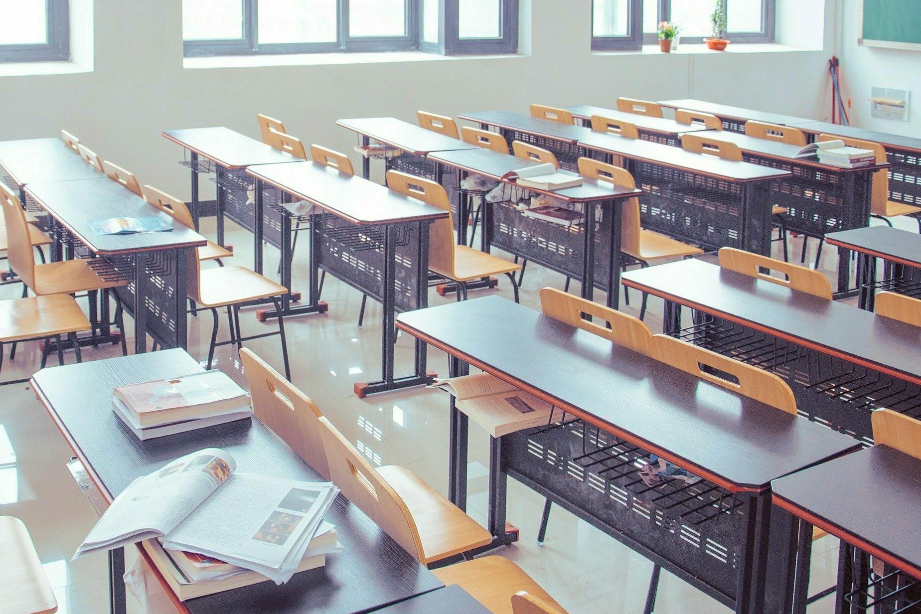 Klassenzimmer mit Tischen, Stühlen und Tafel.