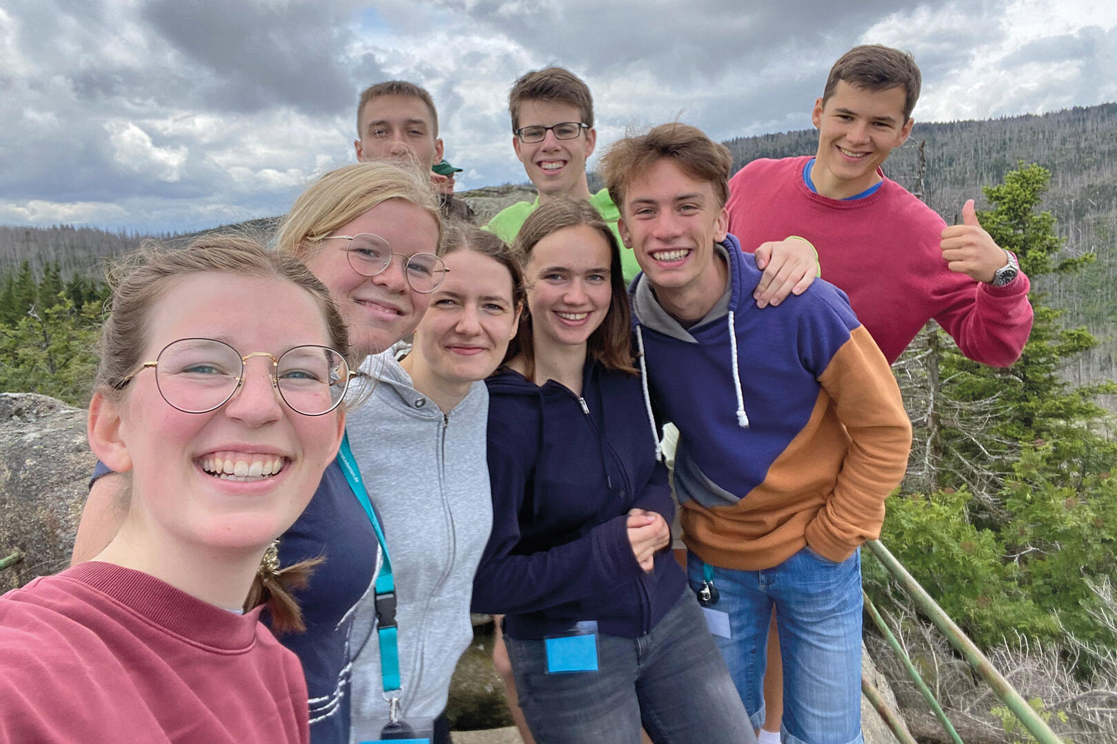 Acht Jugendliche sind lächelnd auf einem Selfie zu sehen, das in der Natur aufgenommen wurde.