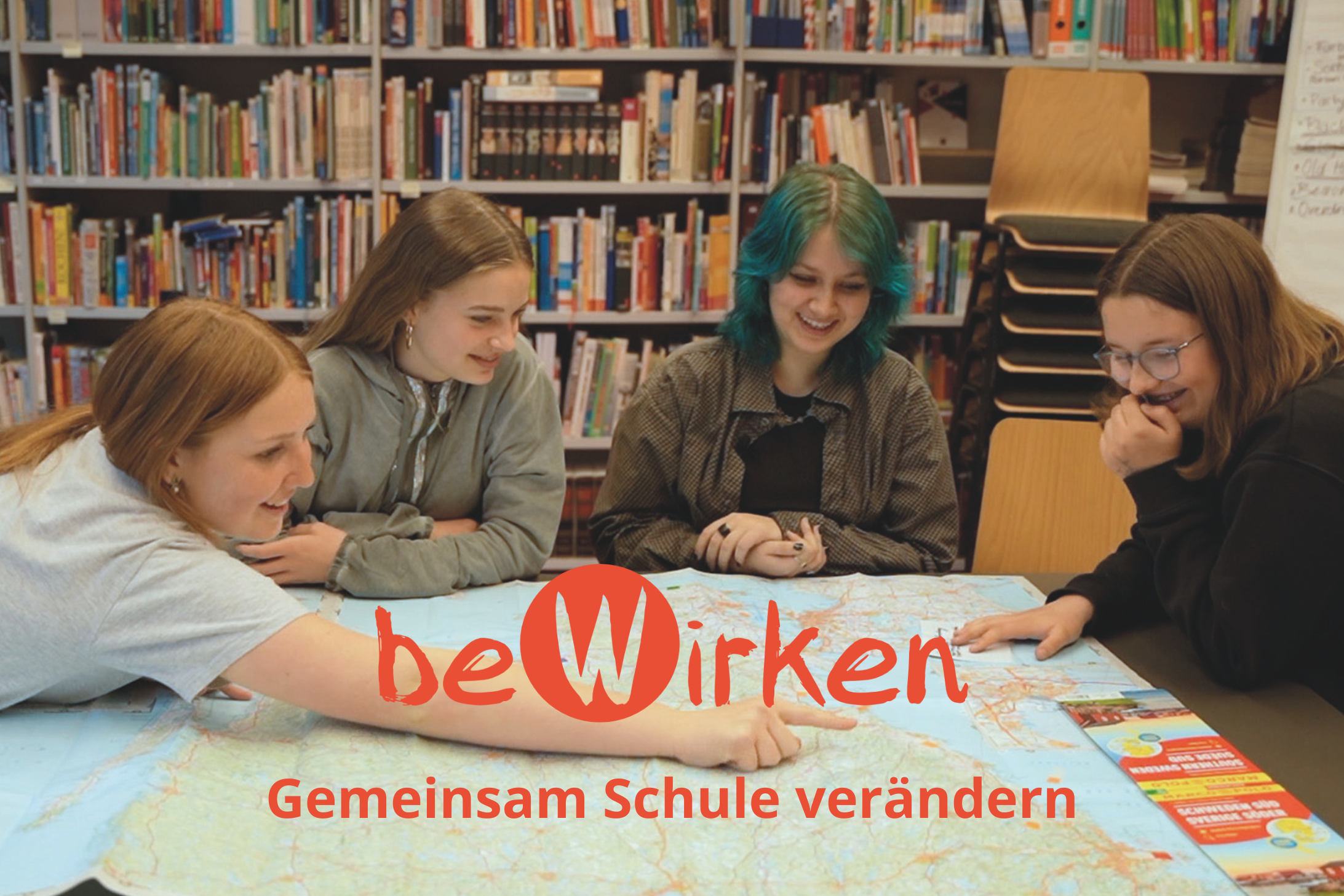 Ein Foto von vier Schülerinnen, die am Tisch sitzen, und gemeinsam auf eine Landkarte schauen. Bewerbung der Organisation beWirken.