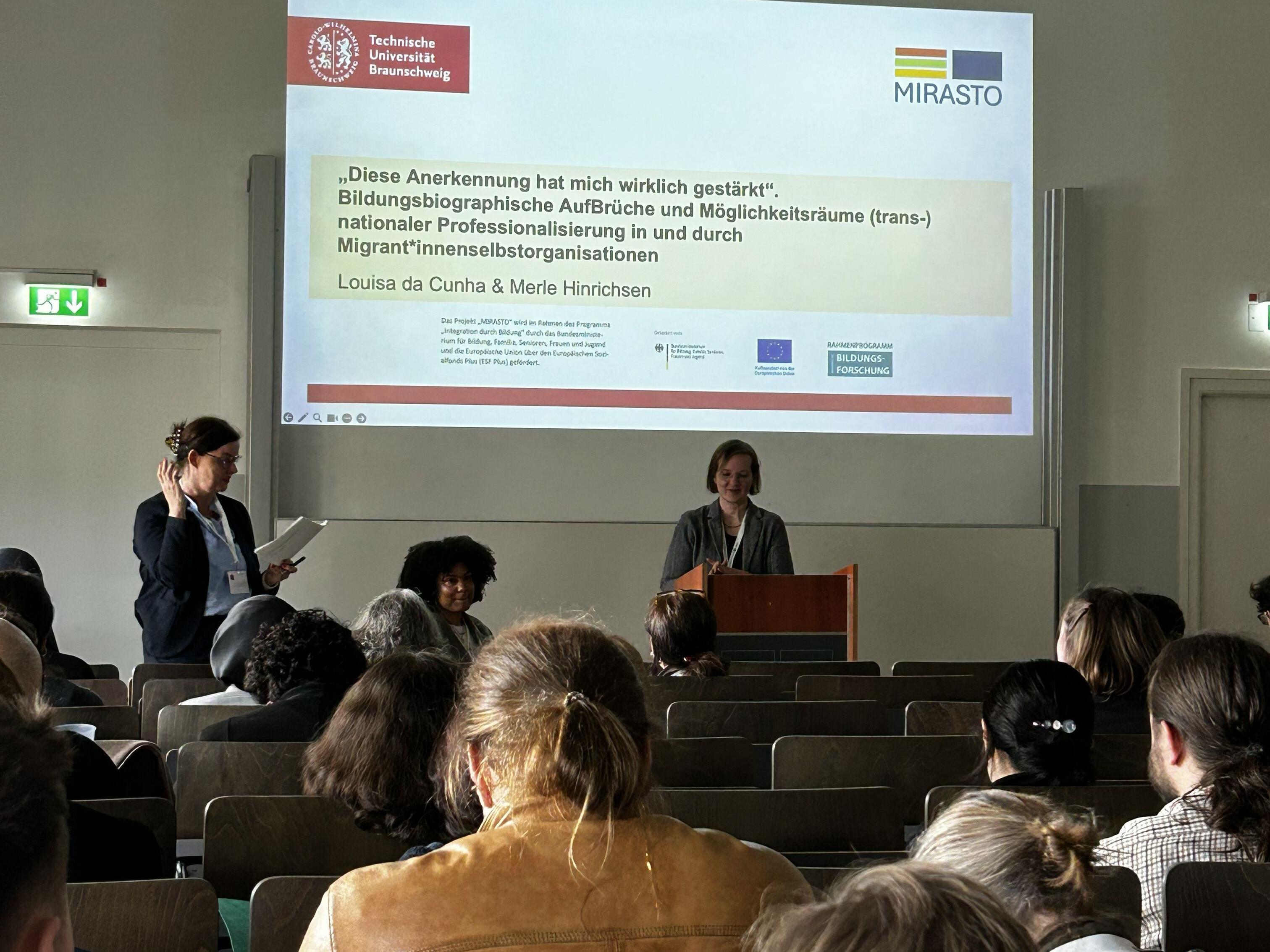 Louisa da Cunha und Merle Hinrichsen halten eine Präsentation im Saal.