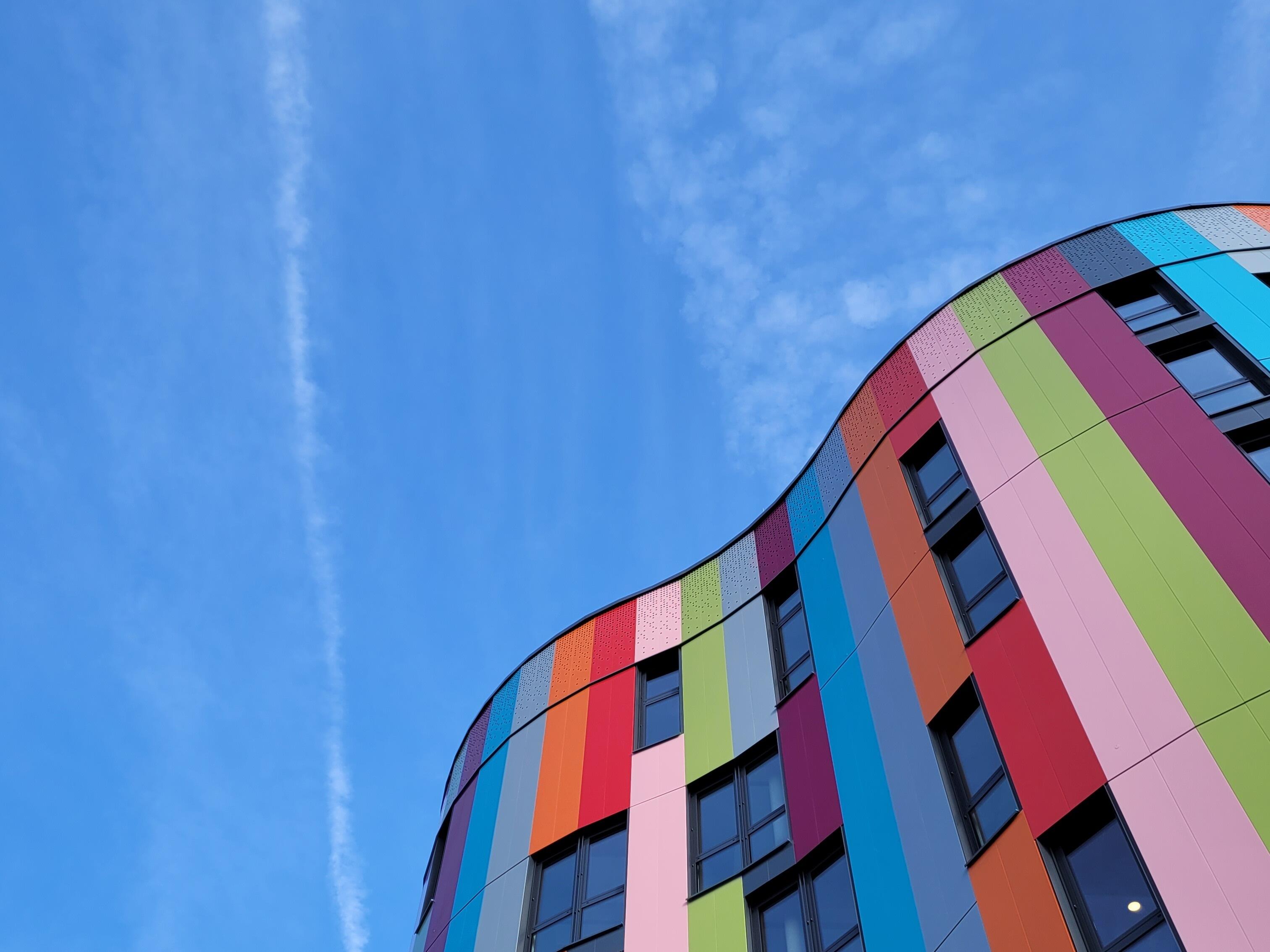Außenansicht des bunten Gebäudes der Junior Uni Daun bei Tag mit blauem Himmel, aufgenommen aus Froschperspektive