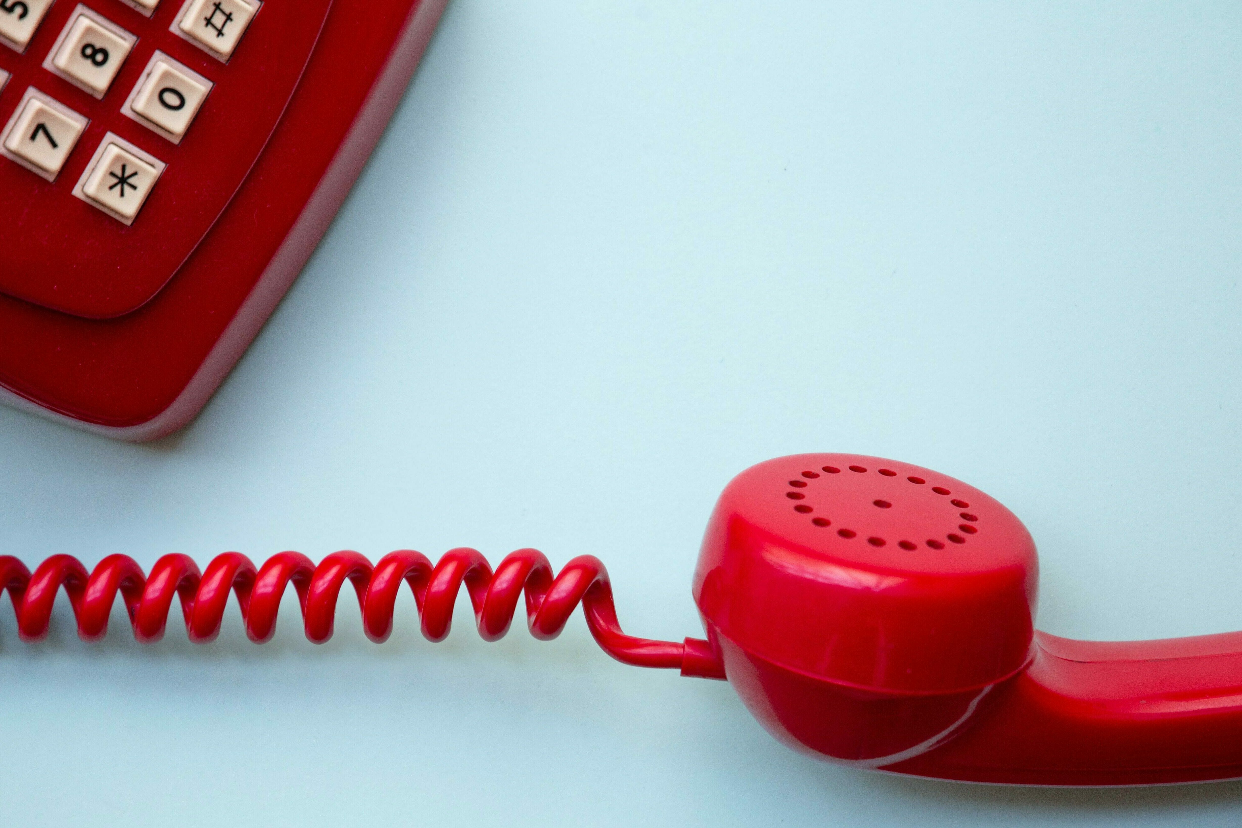 Ein rotes Telefon mit abgehobenem Hörer auf hellblauem Hintergrund.