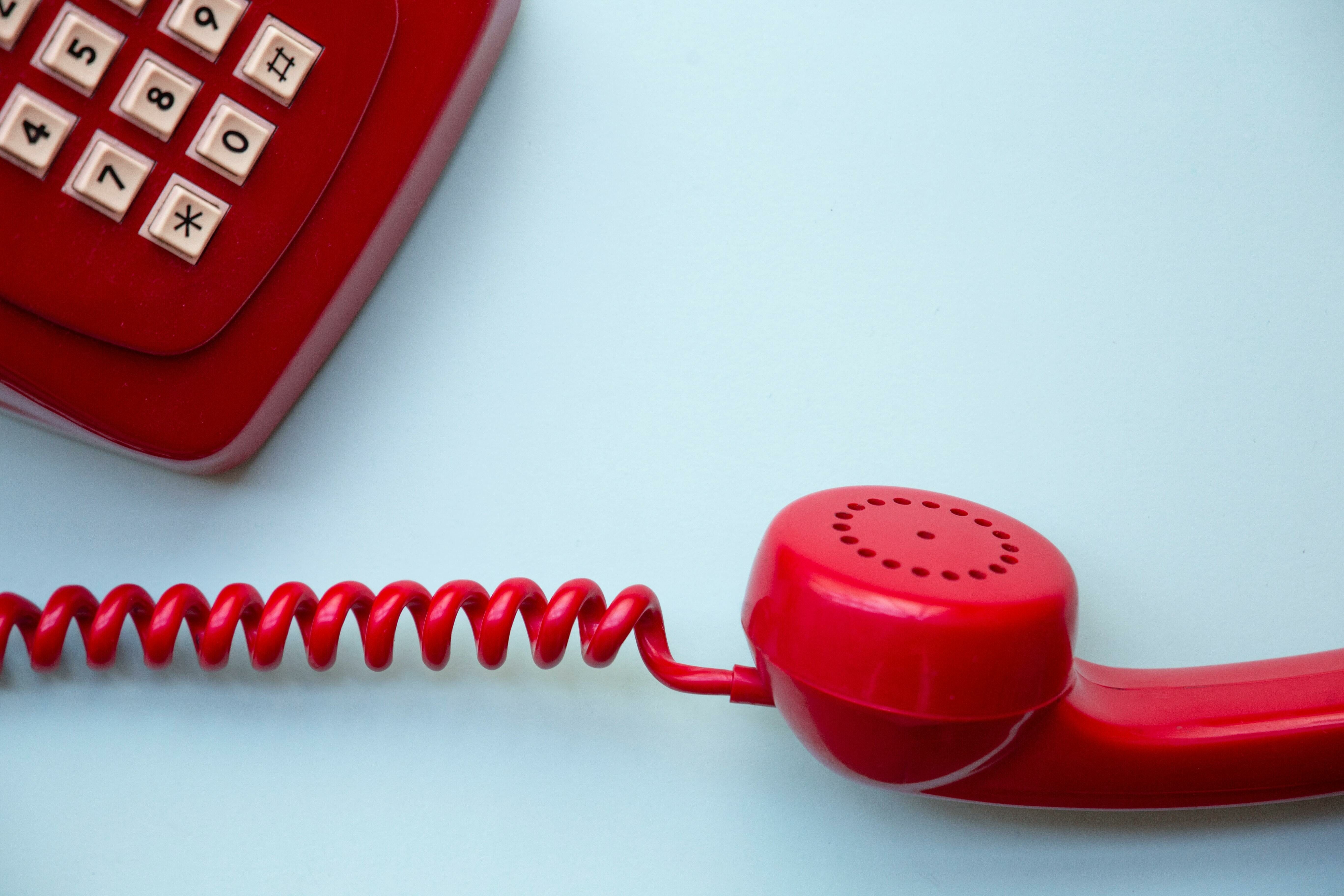Ein rotes Telefon mit abgehobenem Hörer auf hellblauem Hintergrund.