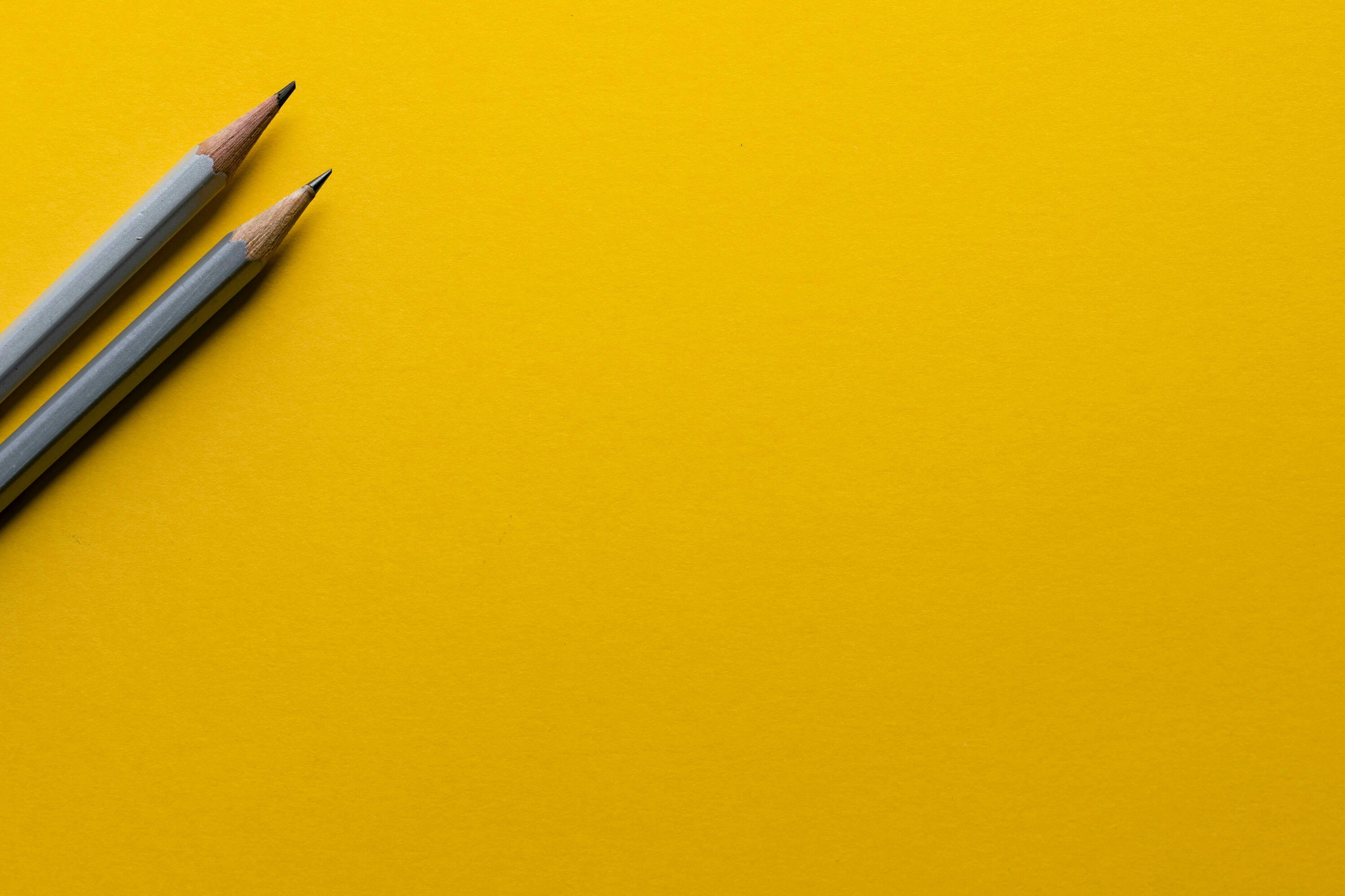 Zwei graue Bleistifte auf gelbem Hintergrund.