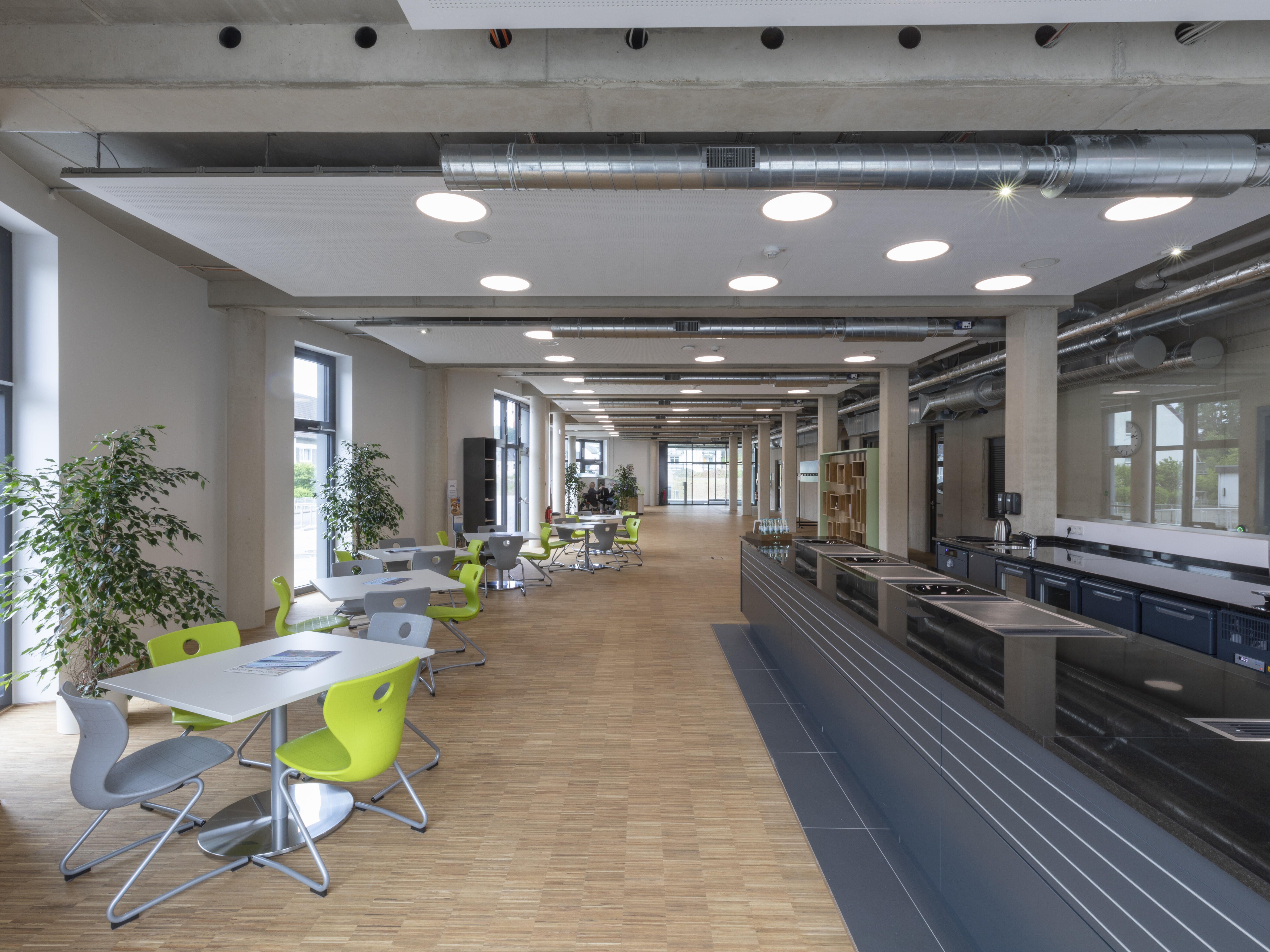 Hinterer Foyerbereich der Junior Uni Daun, mit Vierer-Esstisch-Gruppen und Mensatheke