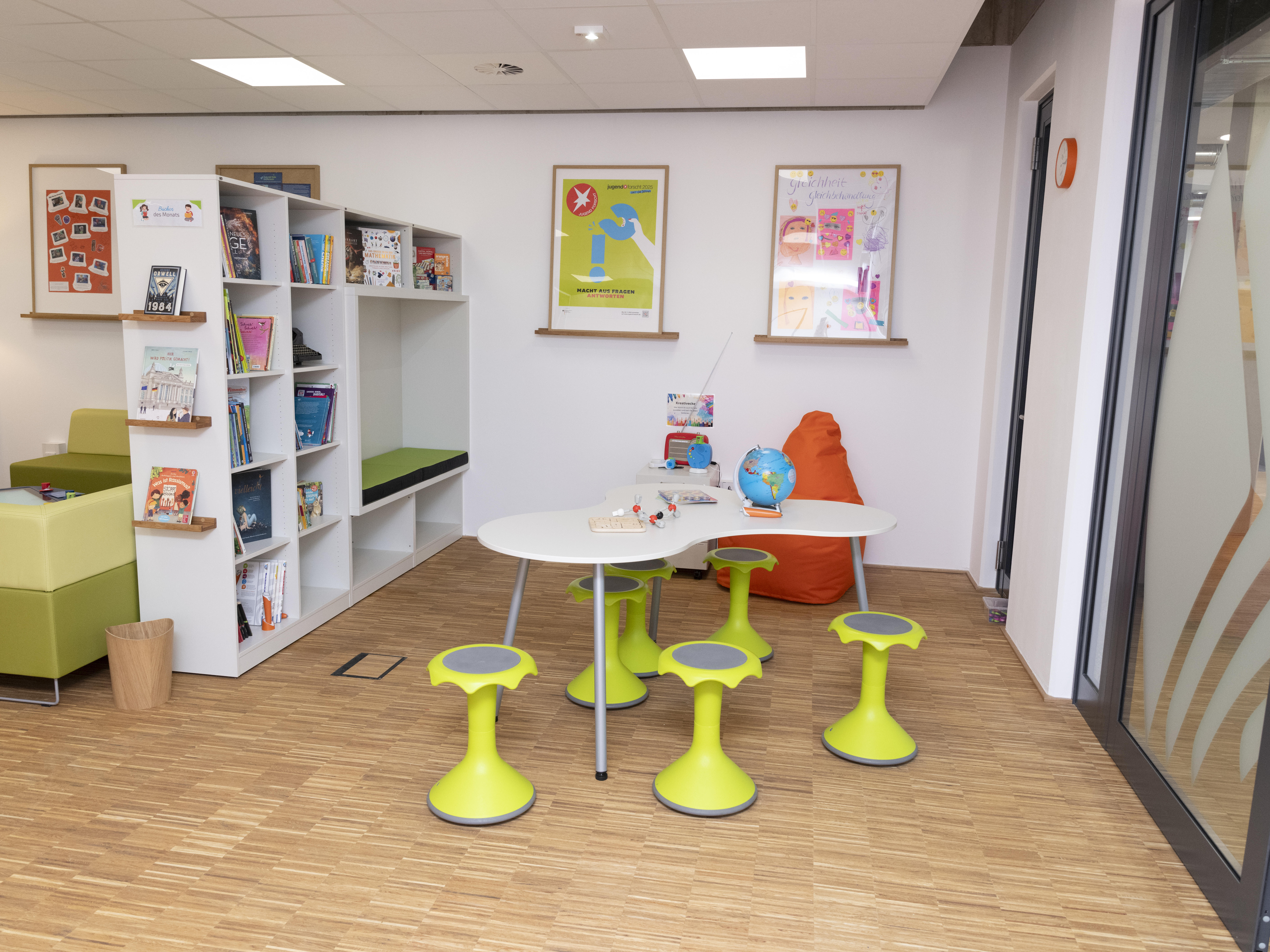 Peters's Corner: Lesebereich im Foyer der Junior Uni Daun mit "Hokki" Wackelhockern, geschwungenem Tisch, Raumteilenden Bücherregal mit integrierer Sitznische.