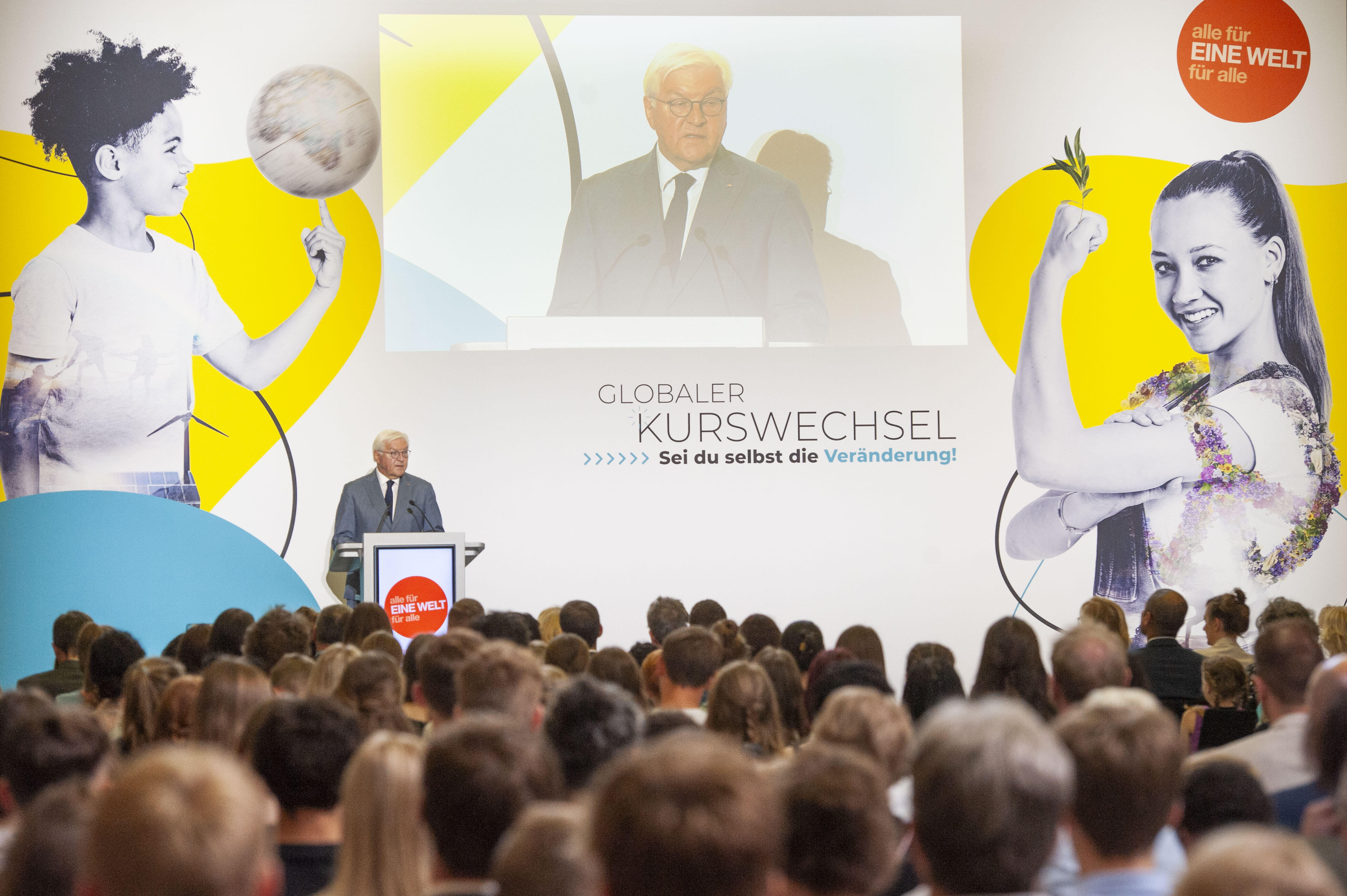 Das Bild zeigte Bundespräsident Frank-Walter Steinmeier, der anlässlich der Preisverleihung zum Schulwettbewerb zur Entwicklungspolitik eine Ansprache auf der Bühne hält. Vor ihm sitzt eine Menschenmenge - Preisträger*innen der Wettbewerbsrunde.