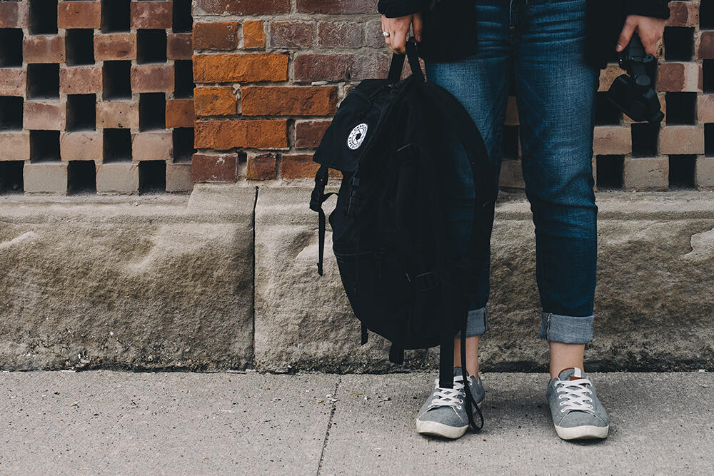 Abbildung der Beiner einer jungen Personen in Jeans mit Rucksack.