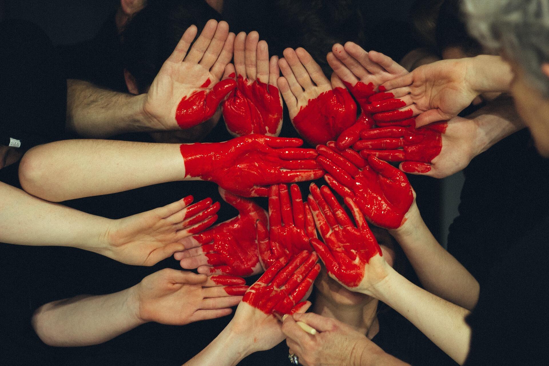 Hände vieler Personen, die sich berühren und auf denen ein rotes Herz aufgemalt ist.