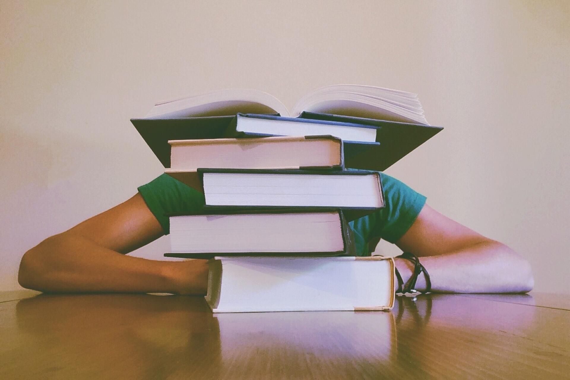 Ein Stapel Bücher auf einem Tisch, dahinter ein Schüler.