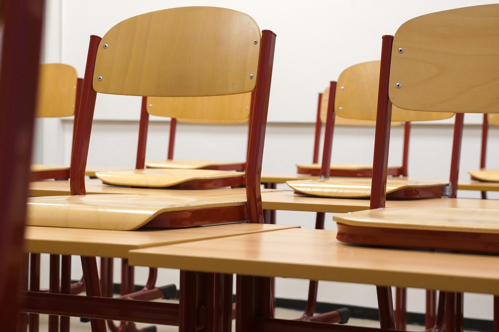 Stühle in einem Klassenzimmer, die auf Tischen hochgestellt sind.