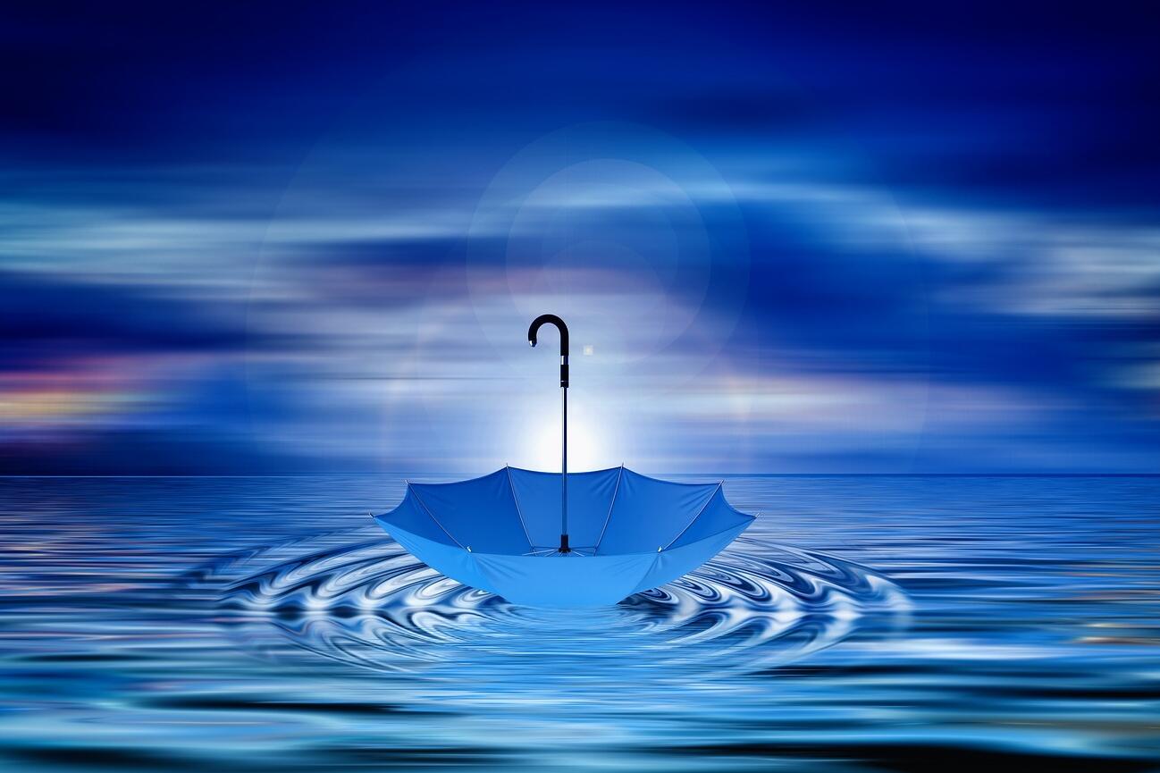 Blaues Wasser vor blauem Horizont und ein blauer Regenschirm, der auf dem Wasser tanzt.