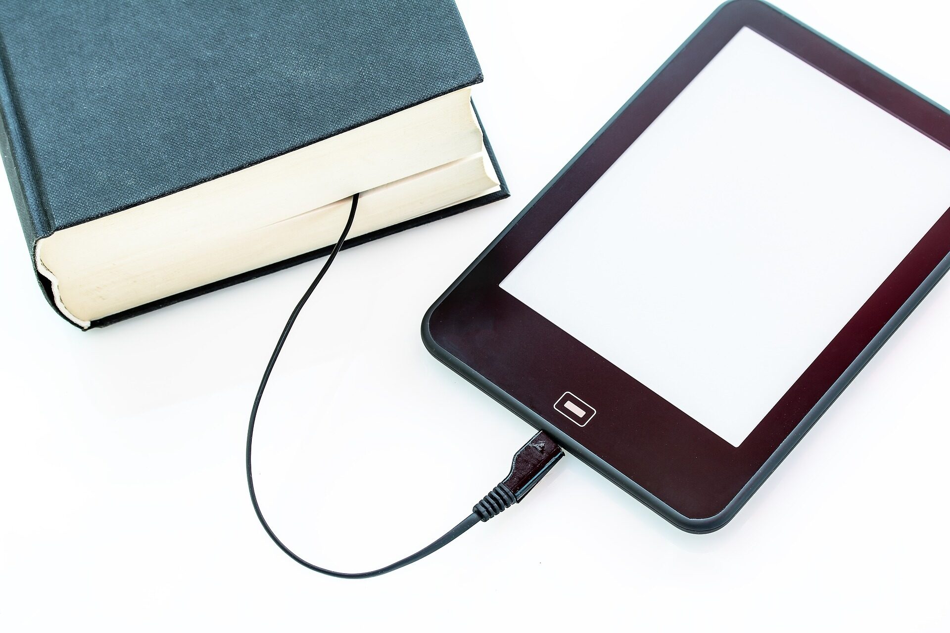 Ein Tablet, das über ein Kabel mit einem Buch verbunden ist zur Veranschaulichung eines eBooks.