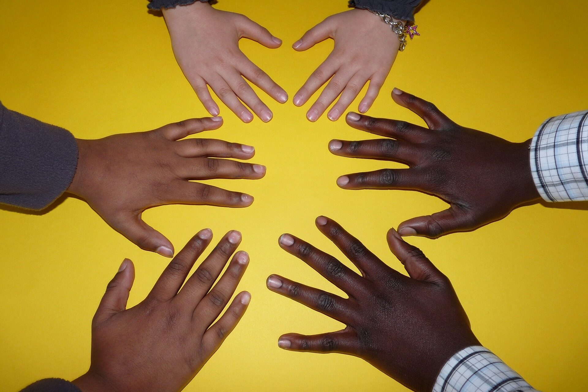 Hände von Kindern mit Migrationshintergrund vor gelbem Hintergrund
