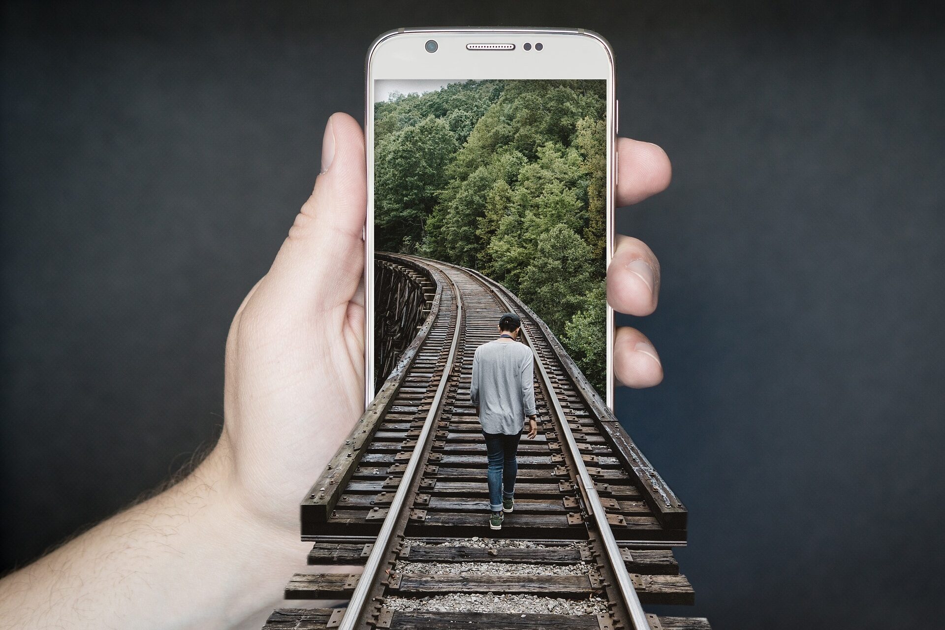 Foto eines Mannes, der auf einer Eisenbahnschiene scheinbar in das Display eines Handys hineinläuft.