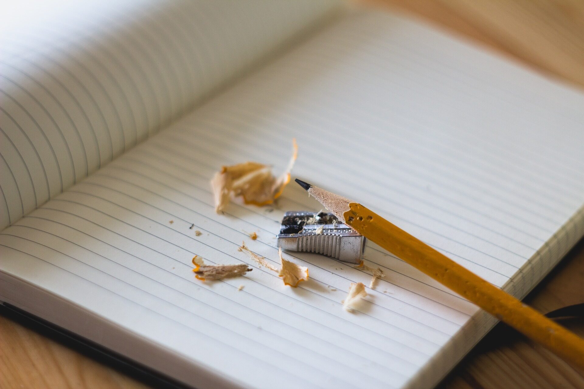 Ein einzelner Bleistift, der angespitzt wird,  liegt auf einem aufgeschlagenem leeres Blatt eines Notizbuches.
