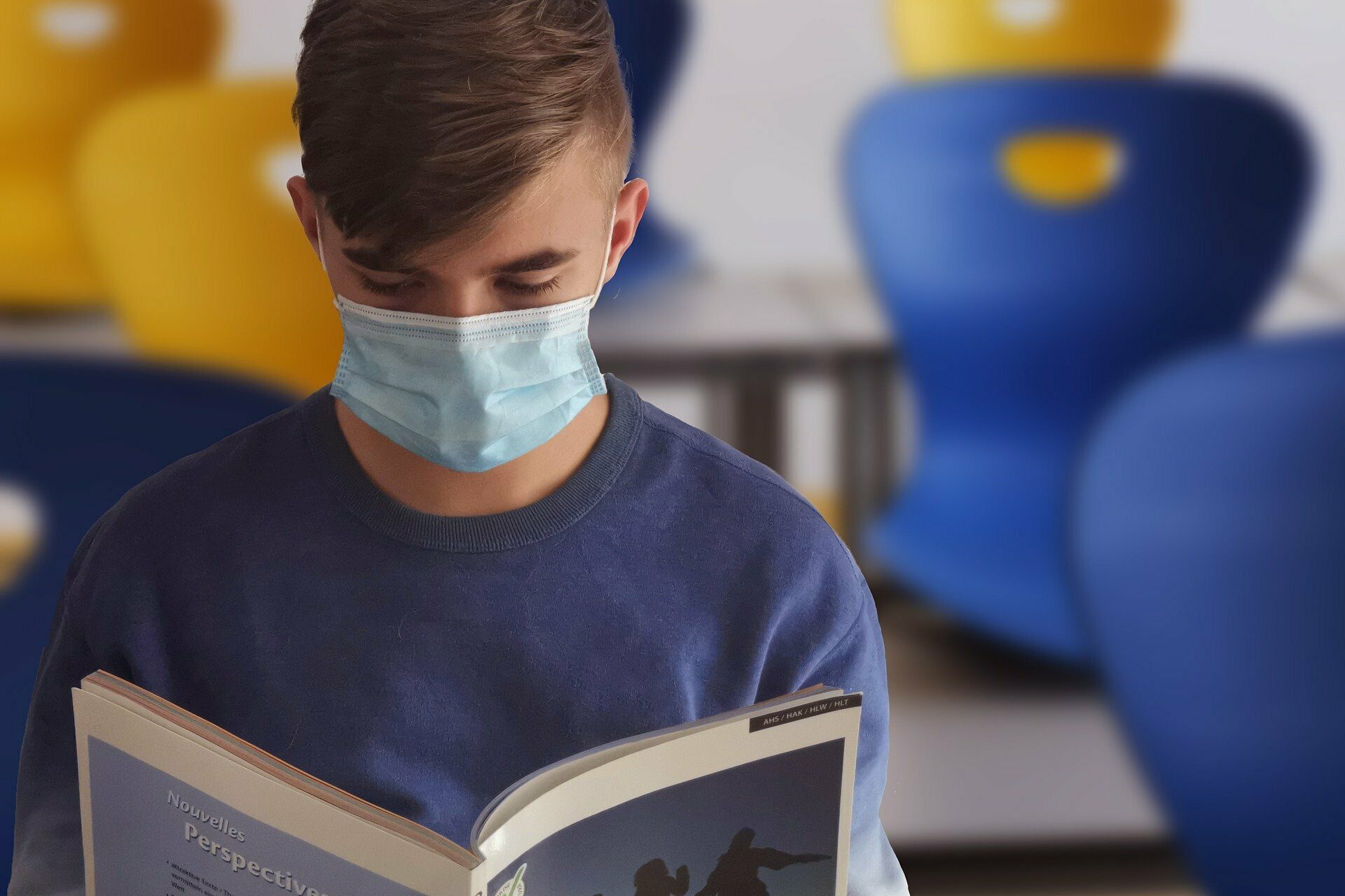 Junge mit Maske liest ein Buch.