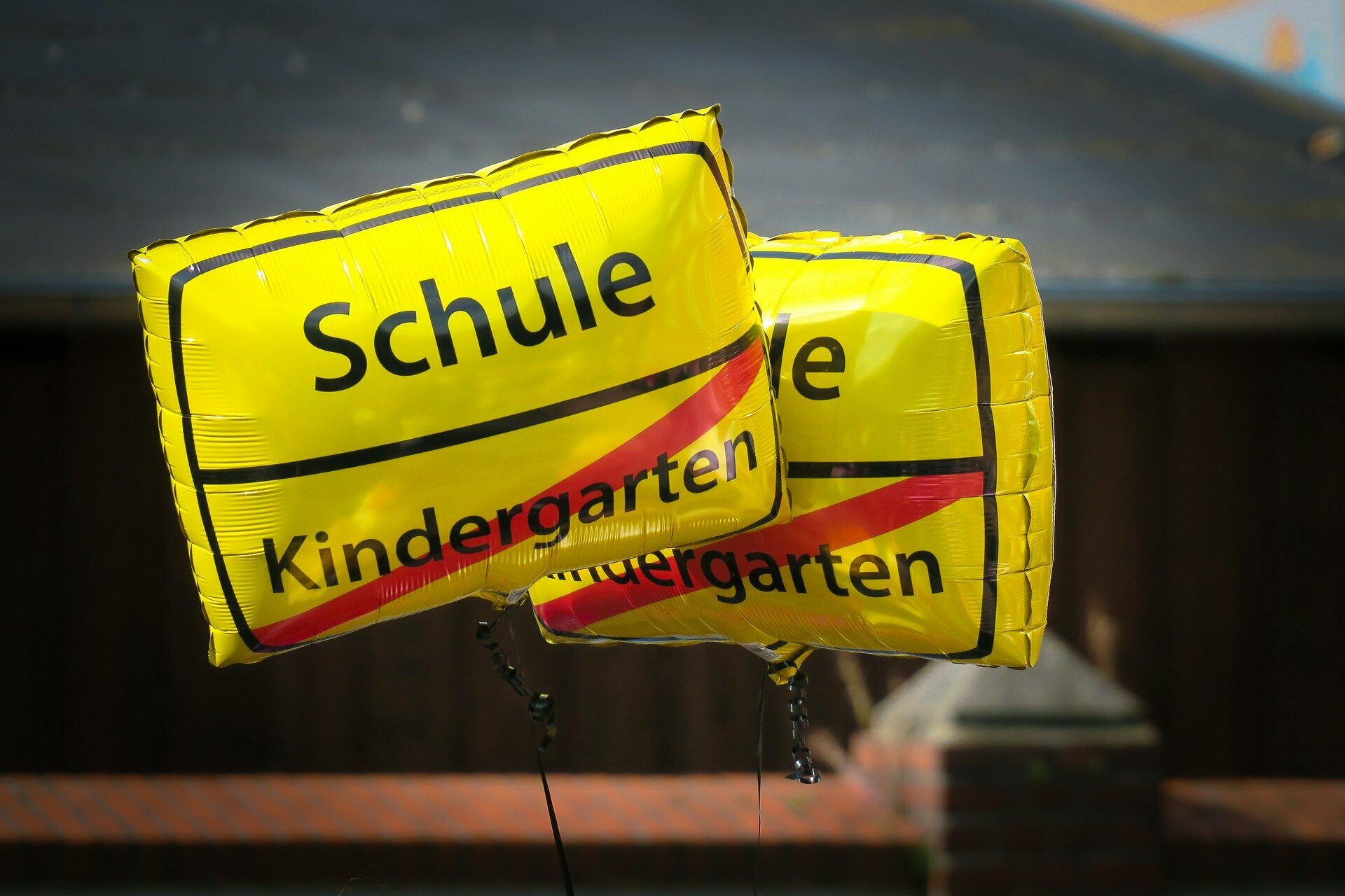 Gelbe Luftballons mit der Aufschrift Schule und dem durchgestrichenen Titel "Kindergarten" als Symbol für die Einschulung.