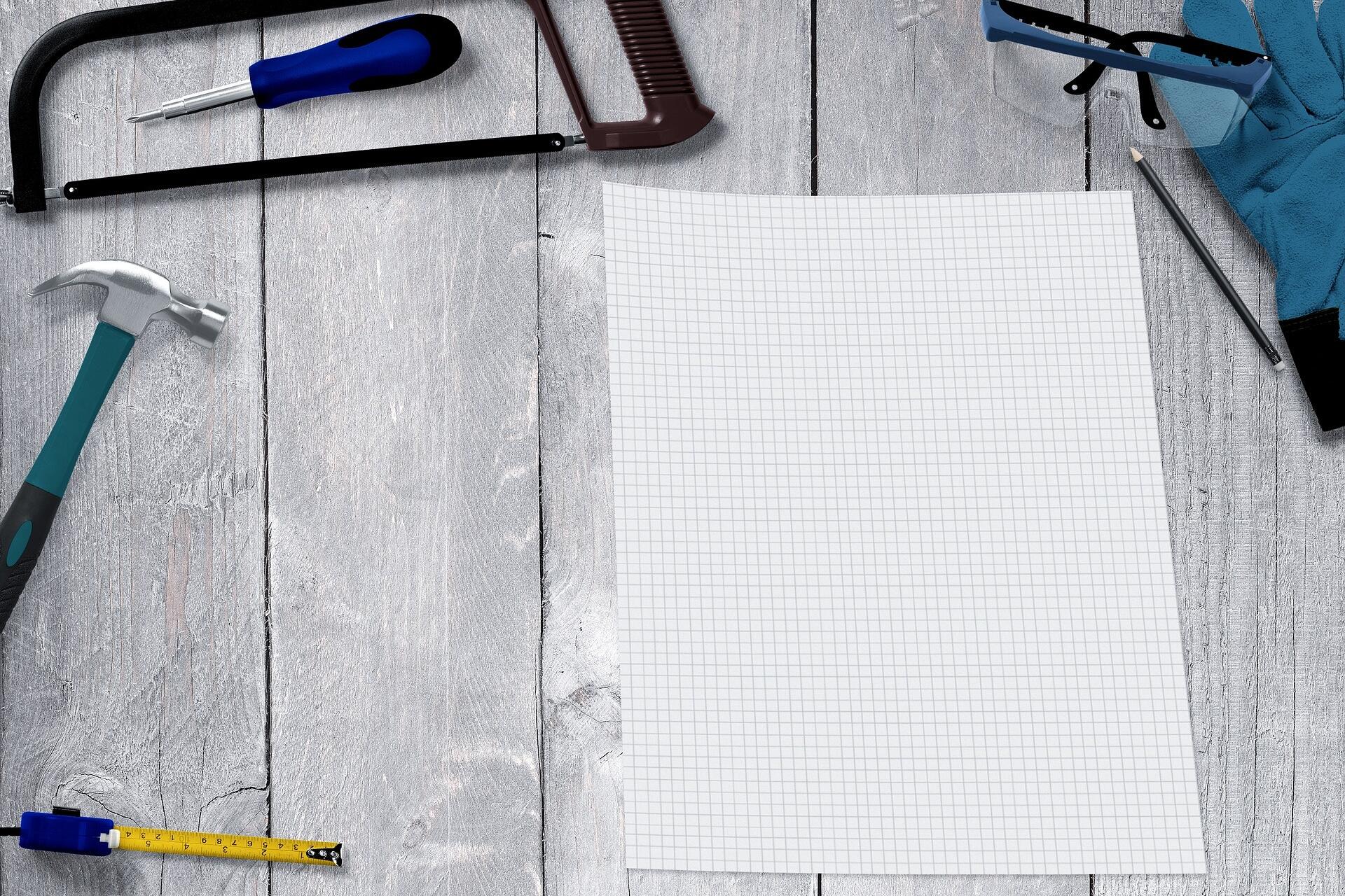 Abbildung von Werkzeug, Stift und Papier auf einem Holztisch zur Veranschaulichung von Handwerksberufen.