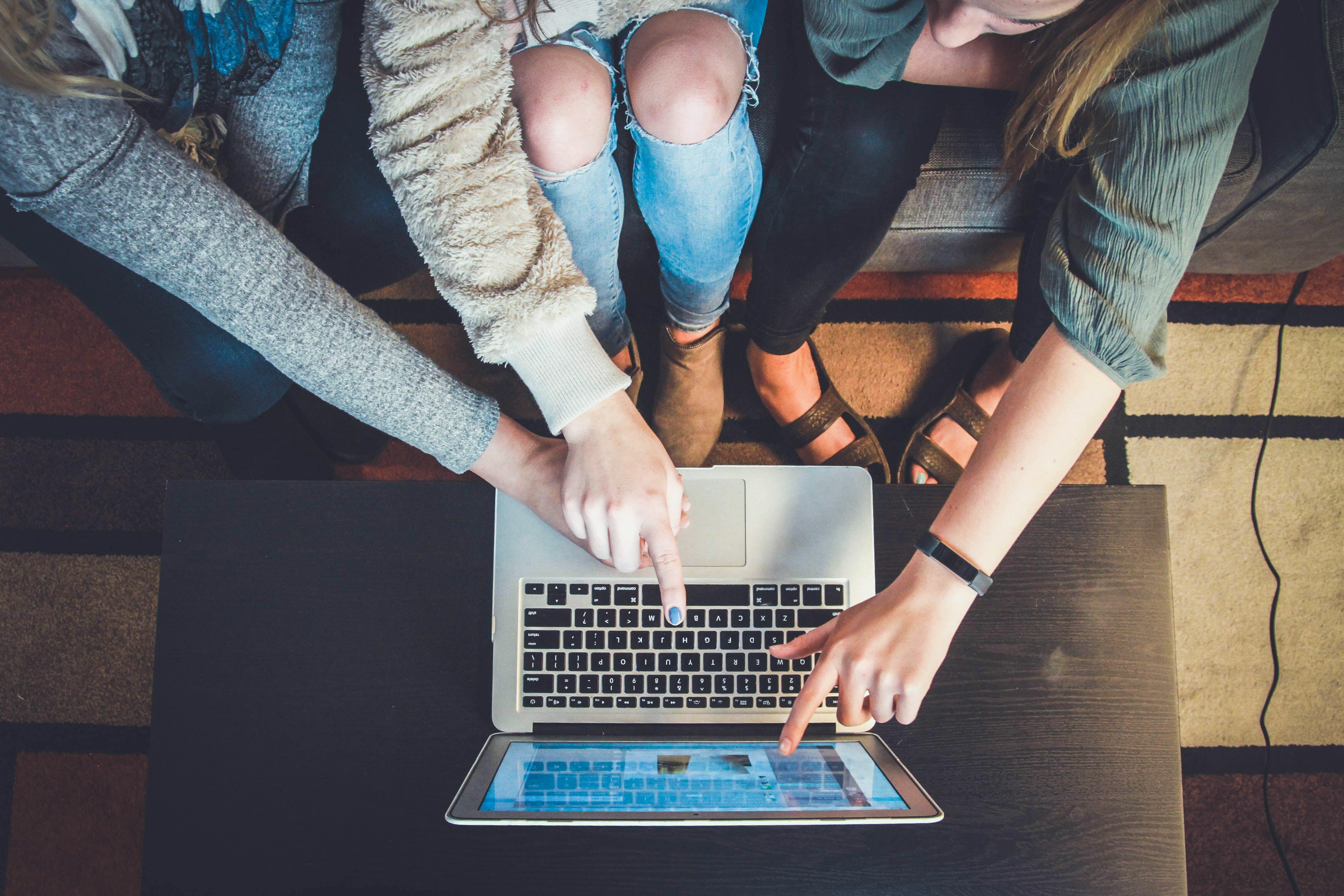 Foto von drei Studenten/Studentinnen, die auf einen Laptop zeigen.